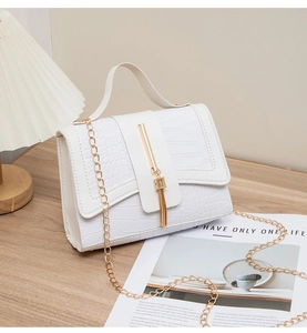 Detail of white crocodile pattern handbag featuring gold chain and tassel on wooden table