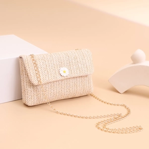Detail of straw woven crossbody bag featuring daisy accent and gold chain strap