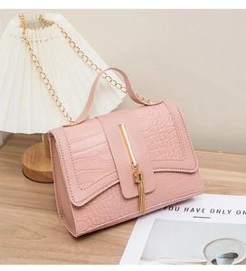 Close-up of pink croc-embossed bag featuring gold tassel charm and metallic chain