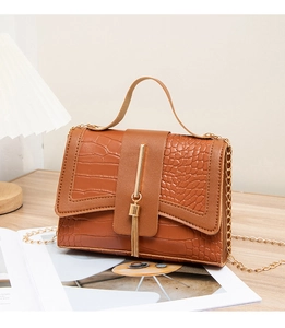 Detail of brown crocodile pattern handbag with gold chain strap on a wooden surface