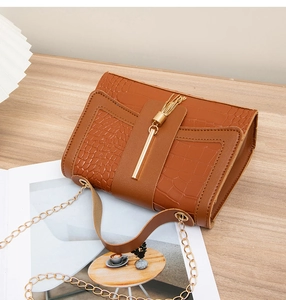 Detail of brown crocodile pattern shoulder bag with gold chain and tassel on wood table