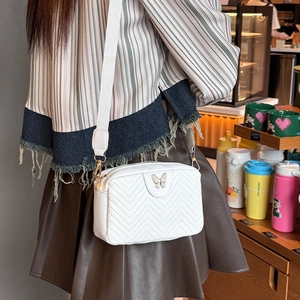 White quilted camera bag with golden butterfly buckle and wide strap on model
