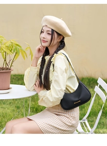 Detail of black lychee grain leather underarm bag with gold logo on model