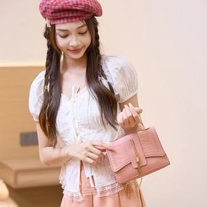 Pink faux croc chain shoulder bag with metal fringe worn by a model in a cozy interior