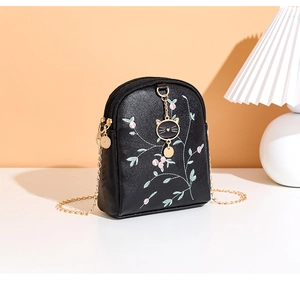Détail du sac à bandoulière en cuir noir avec broderie florale et pendentif chat doré