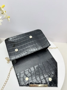 Detailed interior of a black crocodile-pattern square bag with golden chain and magnetic clasp