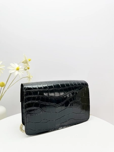 Detail of black crocodile embossed patent leather bag with a luxury gold chain strap
