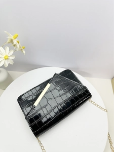 Detail of black crocodile texture bag with gold metal bar and delicate chain strap