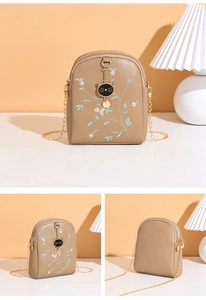 Détail de la broderie florale et du pendentif chat doré sur le sac bandoulière beige