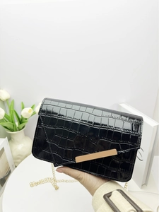 Detail of black crocodile texture bag with gold chain strap on a white table