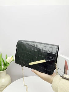 Close-up of black crocodile embossed leather handbag with elegant gold metal bar detail