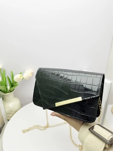 Detail of black crocodile pattern clutch bag with gold bar clasp and metal chain strap