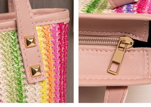 Detail of pink leather handles with gold square studs on a colorful straw tote bag
