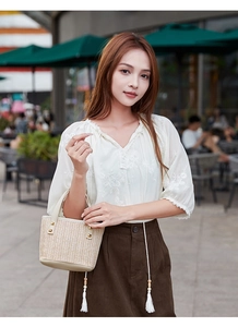 Detail of straw woven handbag with gold square studs held by a model in casual outfit