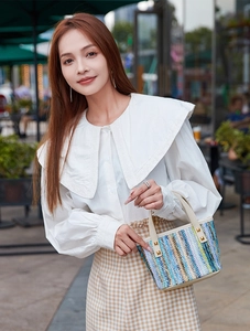 Close-up of multicolored woven straw bag with white leather handle and gold rivet detail
