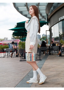 Detail view of a colorful striped woven straw handbag held by a model in casual attire