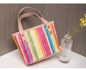 Detail of colorful woven straw tote bag with pink faux leather handle and gold studs