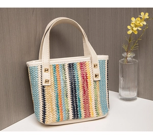 Detail of colorful woven straw bag with gold rivets and ivory leather handles