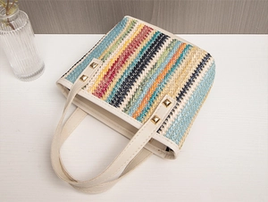 Close-up of colorful straw woven tote bag with bohemian patterns and gold rivets on handle
