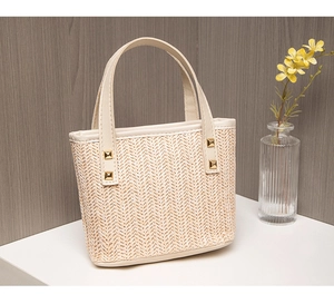 Detailed view of straw handbag featuring V-shape woven texture and gold rivets on handles