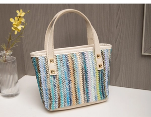 Detail of colorful striped straw tote bag with beige leather handles and gold rivets