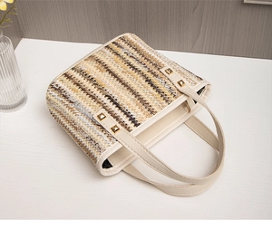 Detailed view of striped straw tote bag featuring creamy leather straps and gold rivets
