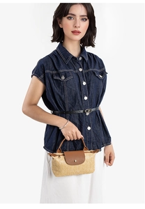 Detailed close-up of straw mini handbag with brown leather flap and metal snap closure