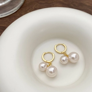 Detail of elegant gold hoop earrings with double pearl pendants on a white ceramic tray