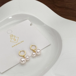 Detail of double pearl drop earrings featuring golden hoops and polished white pearls