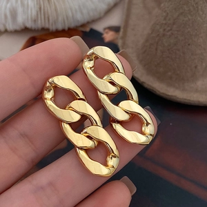 Close-up of chunky gold chain hoop earrings held by hand showing metallic texture