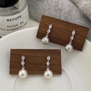 Détail de boucles d'oreilles en perles grises et blanches avec zircon sur présentoir bois