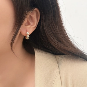 Close-up of gold-plated clover earrings with zircon inlay worn on a model ear