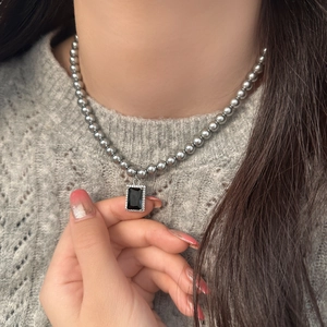 Close-up of grey pearl necklace with rectangular black gemstone pendant on a sweater
