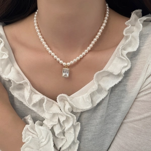 Detail of elegant pearl necklace featuring a rectangular zircon pendant with gold frame