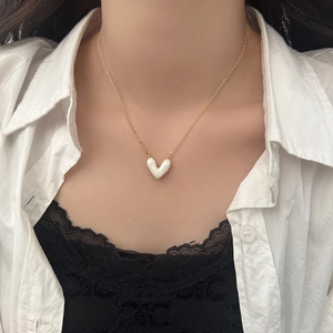 Dettaglio del ciondolo a cuore in smalto bianco con catena dorata minimalista