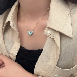Elegante collana con pendente a cuore azzurro su catena dorata indossata su abito neutro