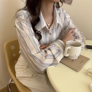 Dettaglio di una collana con ciondolo a cuore abbinata a una camicia a righe blu