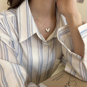 Dettaglio della collana con ciondolo a cuore dorato indossata su una camicia a righe
