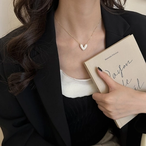 Dettaglio di una collana dorata con pendente a cuore marmorizzato bianco su modella
