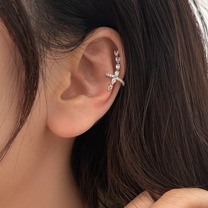 Detailed view of silver ear cuff with sparkling zircons and a small cross charm