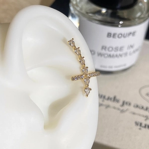 Close-up of a gold cross stud earring with sparkling white zircons on a model ear