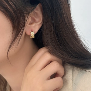 Close-up of gold leaf-shaped earrings with sparkling cubic zirconia worn on ear