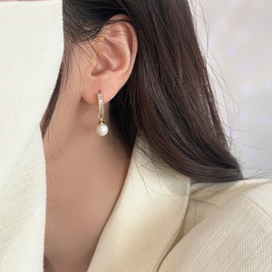 Close-up of elegant gold pearl drop earrings with rectangular zircon studs on ear