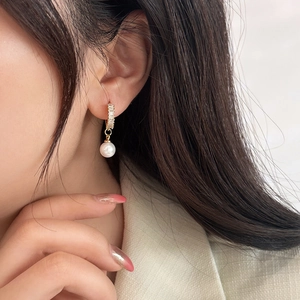 Detail of elegant pearl drop earring with zircon studs shown on model's ear