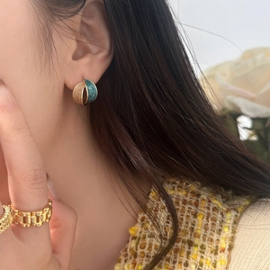 Close-up of dual-tone champagne gold and marble blue enamel earrings on a model