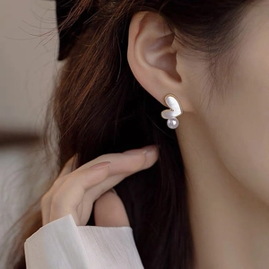 Elegant heart shell stud earrings with hanging pearl and golden base worn by a model