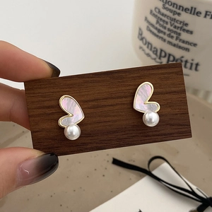 Elegant heart shell pearl earrings in gold finish presented on a wooden display board