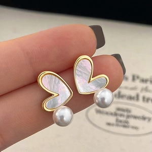 Close-up of heart-shaped shell earrings with white round pearls and gold metallic frames