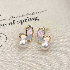 Detailed macro view of heart-shaped gold earrings with iridescent shell and white pearl