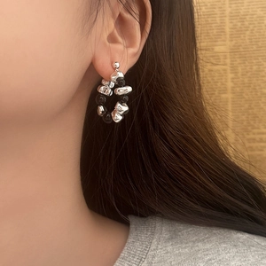 Detail view of irregular silver beads and black stone hoop earrings worn by a model